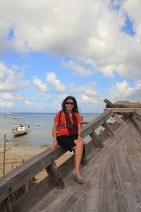 Woman sitting on wood against sky