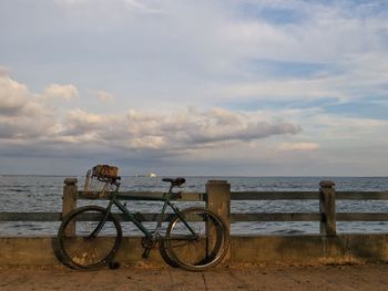Bicycle parked by calm sea against the sky
