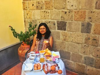 Portrait of woman with breakfast served on table against wall