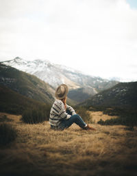 Man sitting on mountain against sky