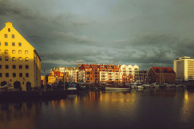 Buildings by river against sky in city