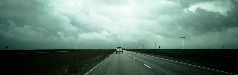 Vehicles on road against storm clouds