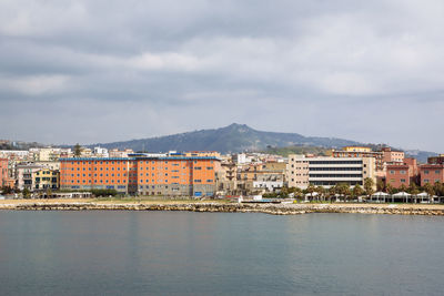 Buildings in city by sea against sky