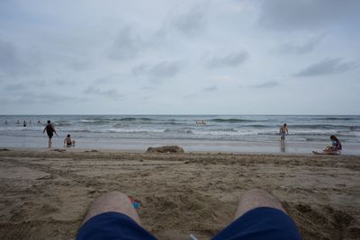 Low section of people on beach against sky