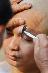 Cropped hand of man cutting eyebrow of monk during ordination