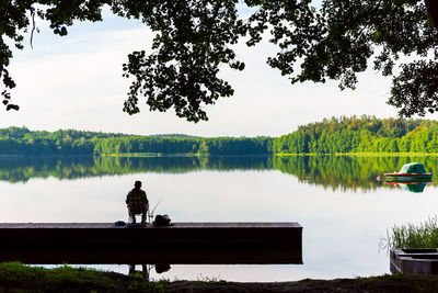 People sitting by lake against sky