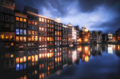 Illuminated buildings by river against sky at night