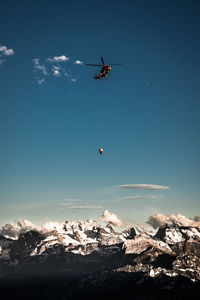 Low angle view of helicopter flying over snowcapped mountain against sky