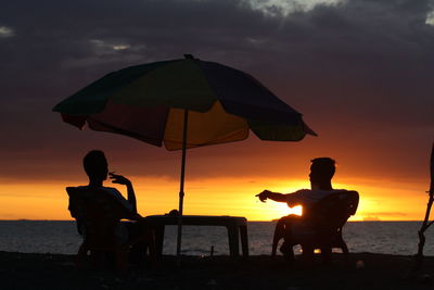 Silhouette people sitting on beach during sunset