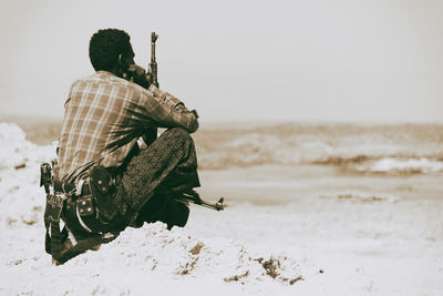 Rear view of man sitting at beach against sky