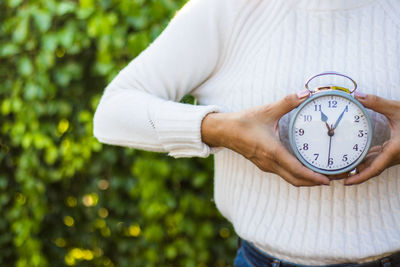 Close-up of woman holding clock against blurred background