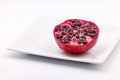 Studio shot of half a pomegranate striking red exposed on a white plate cut out on white background