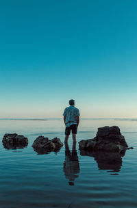 Rear view of man standing on rock against sea