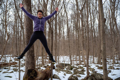 Full length of woman jumping in snow covered woods