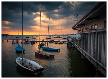 Sailboats moored at harbor against sky during sunset