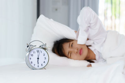 Woman with alarm clock sleeping on bed at home