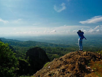 Man standing on rock looking at mountains against sky