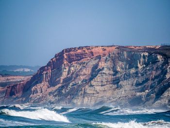 Scenic view of cliff by sea against clear sky