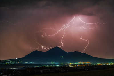 Lightning over illuminated mountain against sky at night