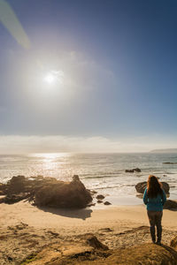 Rear view of woman standing on beach against sky