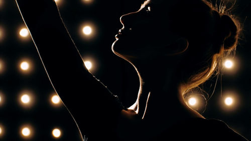 Close-up of silhouette woman dancing against illuminated lights
