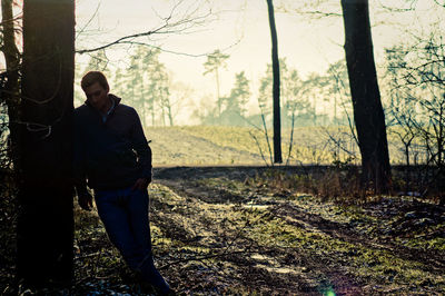 Sad man standing by tree at forest