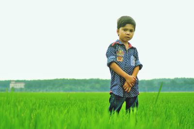 Portrait of boy standing on field against clear sky