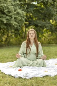 White pretty pregnant woman meditates in park, sits on blanket, stress relief,mindfulness. enjoying