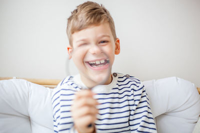 Portrait of smiling boy holding magnifying glass while sitting on sofa