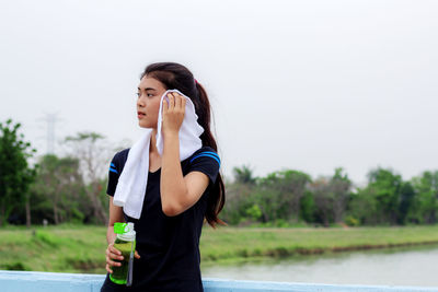 Side view of young woman drinking water against clear sky