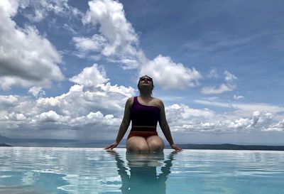Woman sitting in infinity pool against sky