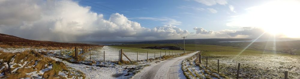 Panoramic view of road amidst field against sky