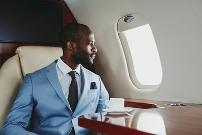 Young businessman looking through window while traveling through private jet