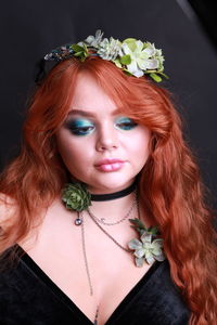 Sensuous young woman wearing wreath and necklace against black background