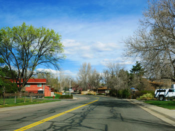 Road by trees and houses against sky