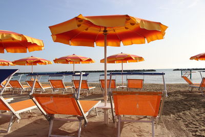 Orange chairs and tables on beach against sky