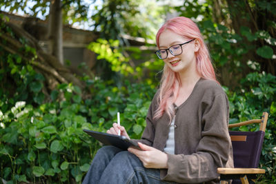 Young woman using mobile phone while sitting against trees