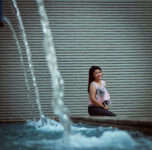 Portrait of young woman sitting by fountain