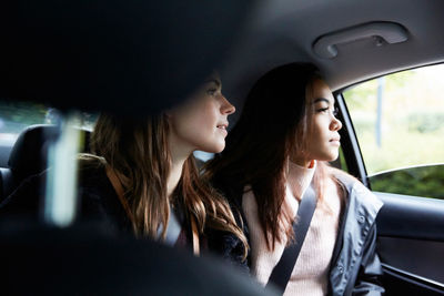 Female friends looking through window while sitting in taxi at city