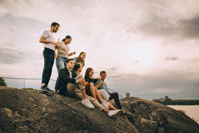 People sitting on rock against sky