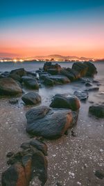 Rocks on beach against sky during sunset