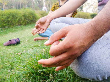 Midsection of man with woman meditating while sitting on grassy field in park