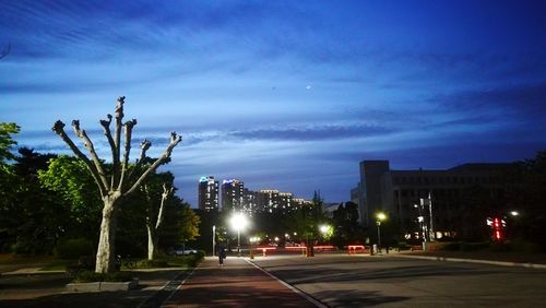 Illuminated street by buildings against sky at dusk