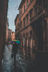 Rear view of man walking on wet street amidst buildings