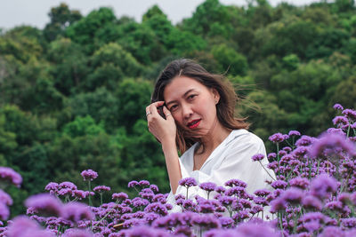 Portrait of beautiful woman standing by purple flowering plants