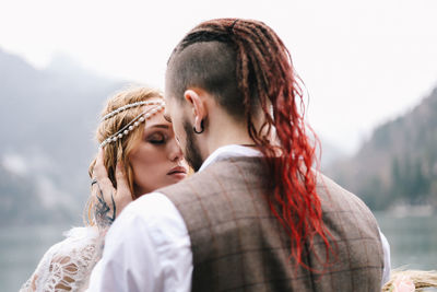 Two happy people in love the bride and groom in wedding outfits embrace by the lake and mountains