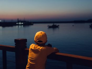 Rear view of boy standing by railing against sky during sunset
