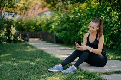 Full length of woman using phone while sitting on grass