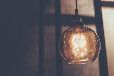 Close-up of illuminated light bulb hanging against wall