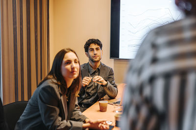 Male and female business professionals listening to colleague in meeting at office